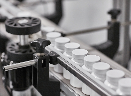 A close-up of a production line featuring white bottles in a factory, with machinery involved in the bottling process.